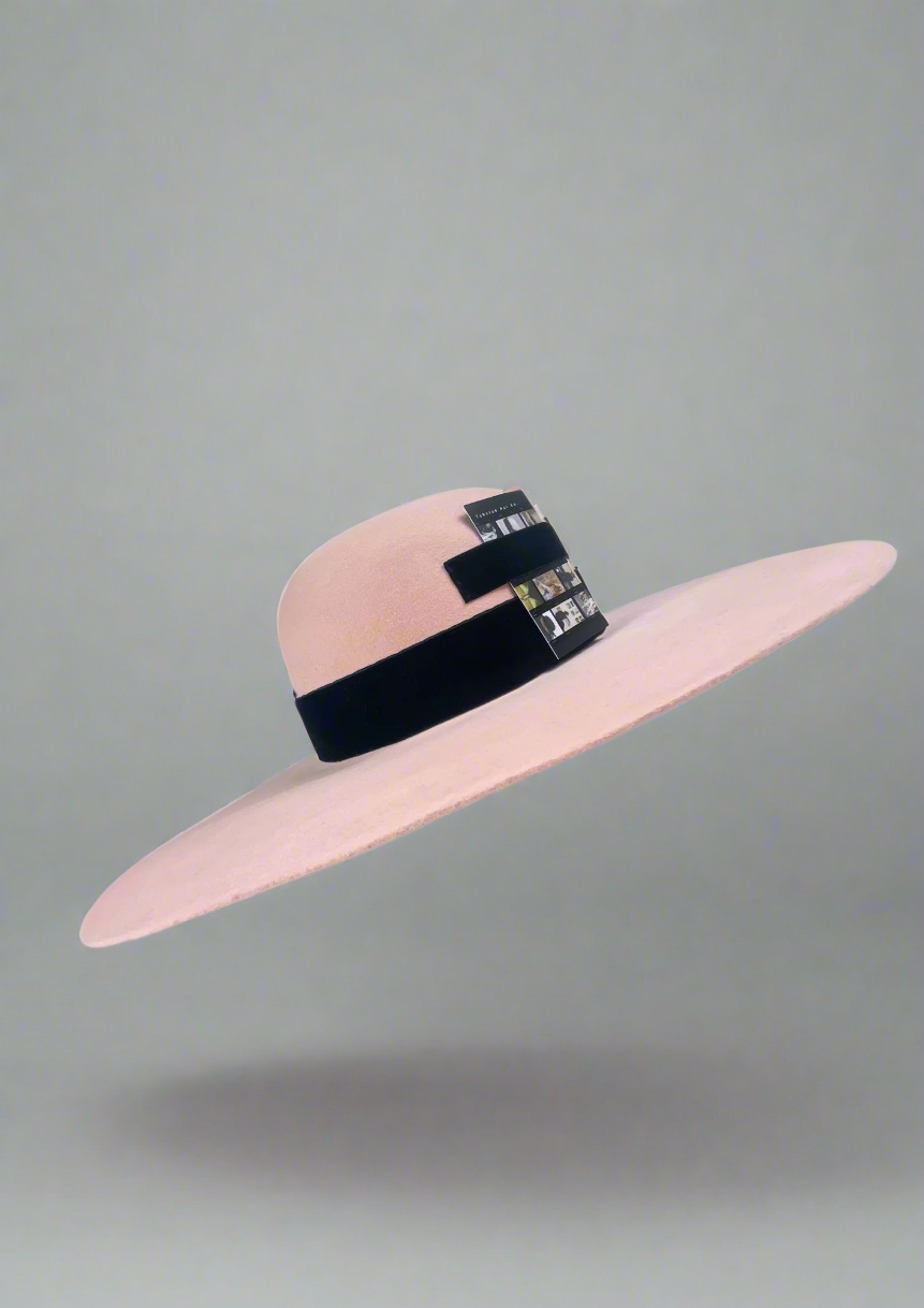 Pink wide-brimmed hat with a black ribbon on a white background