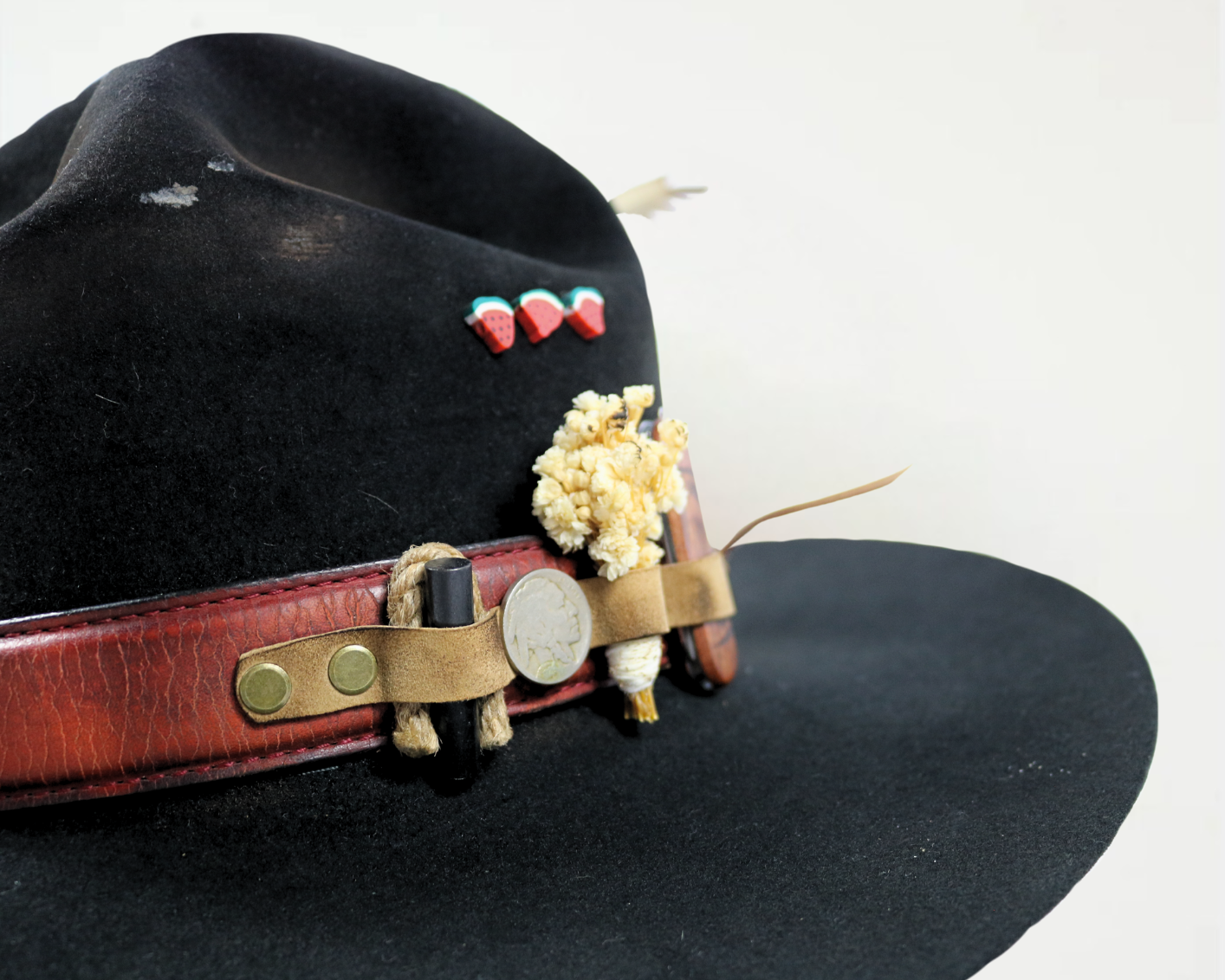 Black hat with decorative band featuring flowers and heart-shaped buttons on a white background