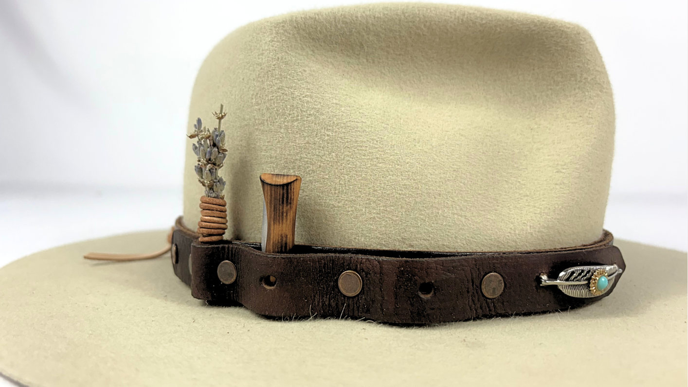 Beige cowboy hat with a brown leather band featuring decorative elements on a white background