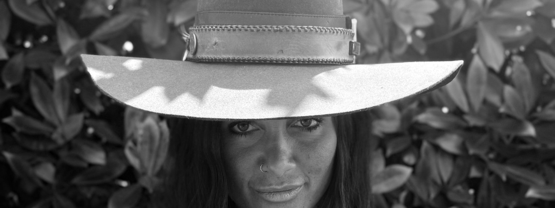 Black and white photo of a person wearing a wide-brimmed hat with leaves in the background