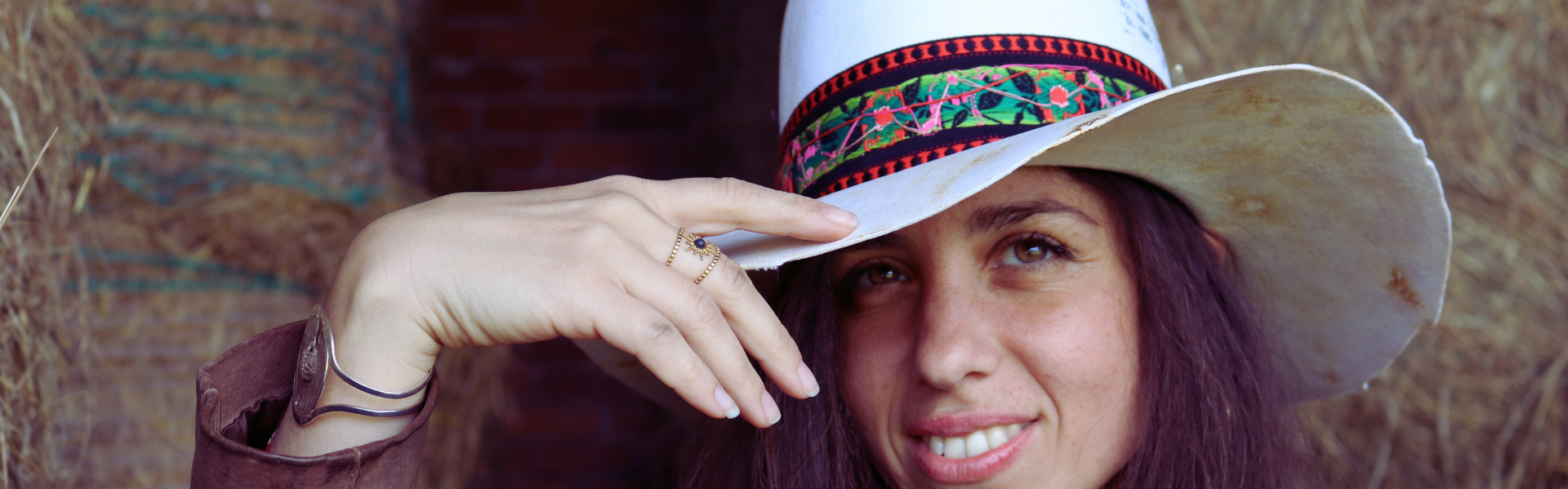 Woman wearing a white hat with a colorful band, posing against a textured wall.