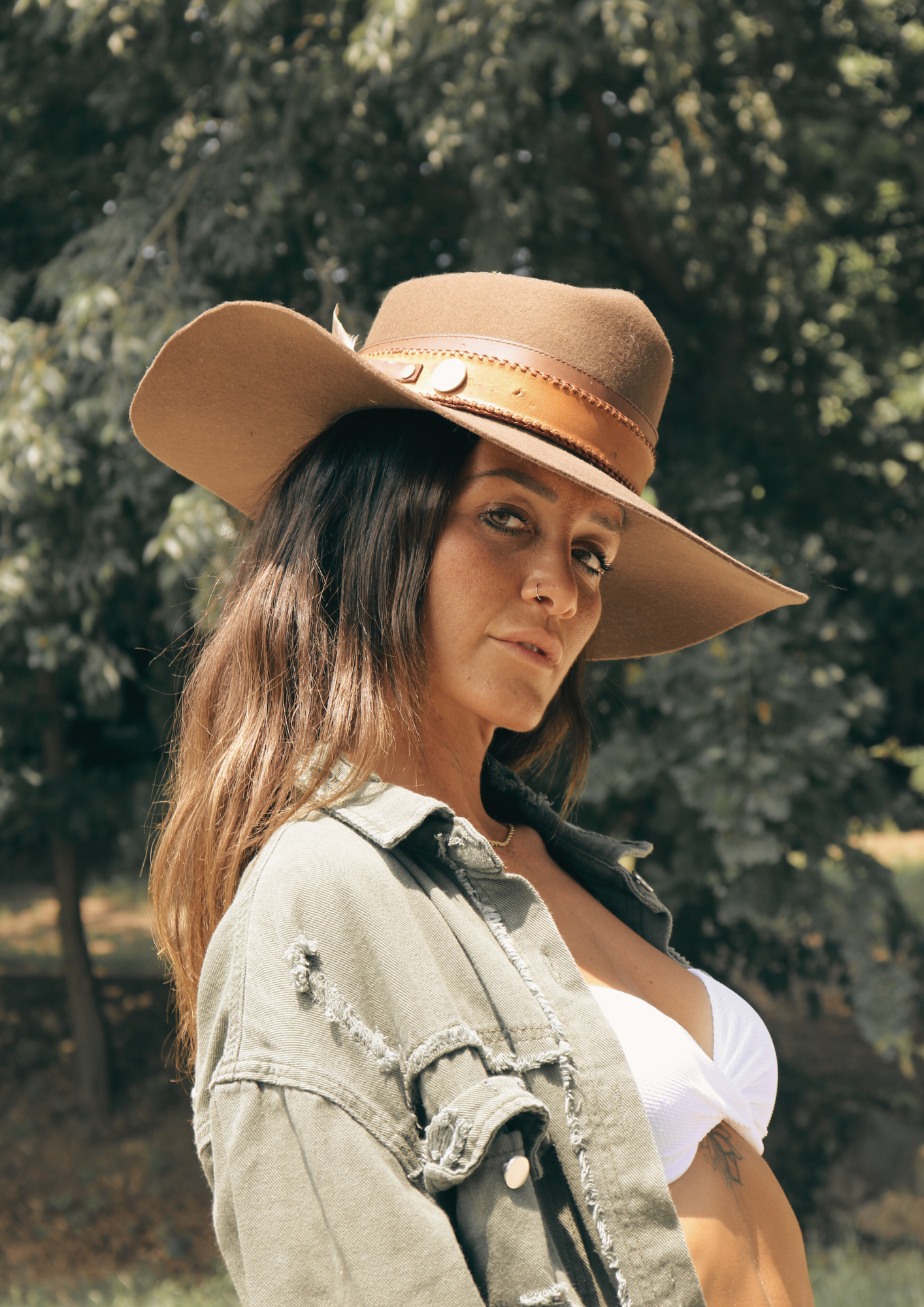 Woman wearing a brown cowboy hat outdoors with trees in the background