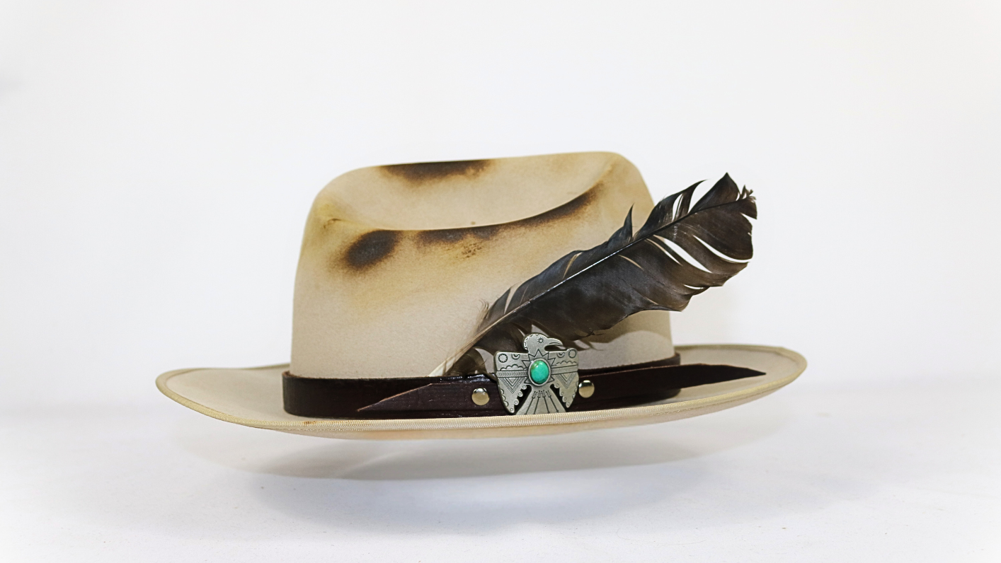 Worn leather hat with feather and band on a white background