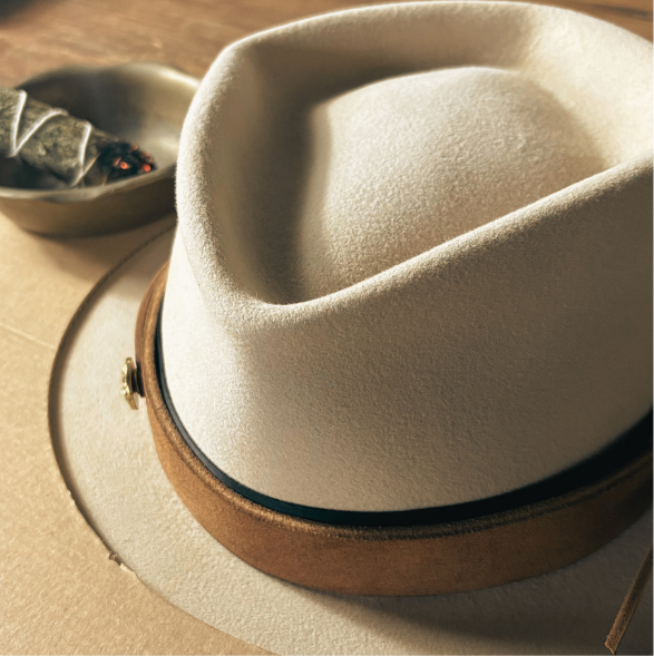 Beige diamond crown felt hat with brown leather band on a wood background with sage burning in metal bowl