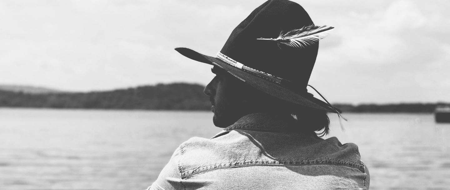 Person wearing a hat with a feather, standing by a body of water.